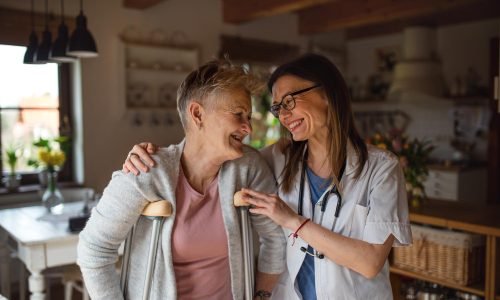 front-view-healthcare-worker-caregiver-visiting-senior-woman-indoors-home-helping-her-walk